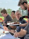 four people sitting at a table smiling with another person standing behind them serving them food